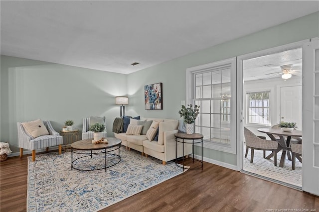 living area featuring a ceiling fan, visible vents, baseboards, and wood finished floors