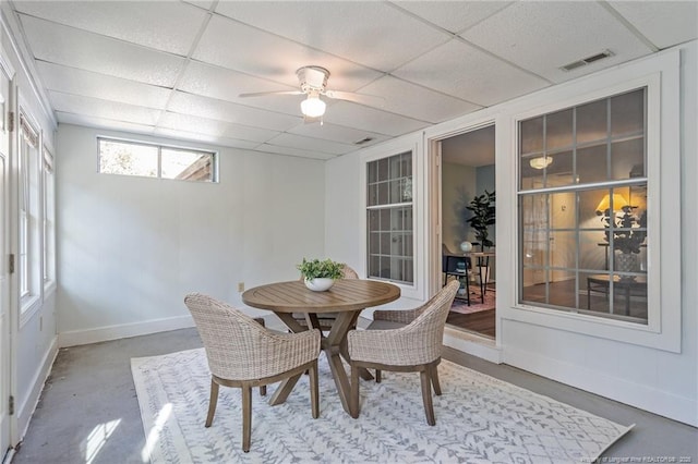 dining space featuring concrete floors, a drop ceiling, a ceiling fan, and baseboards