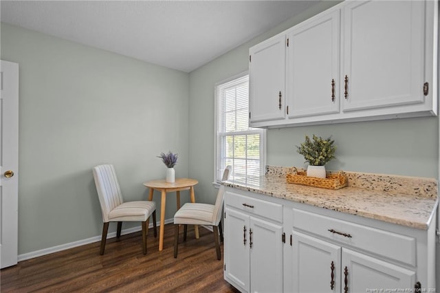 kitchen featuring light stone counters, dark wood finished floors, white cabinetry, and baseboards