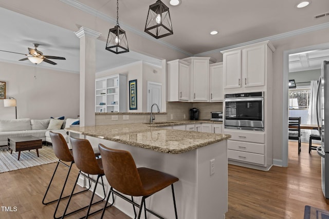 kitchen with white cabinetry, sink, a breakfast bar area, stainless steel oven, and kitchen peninsula