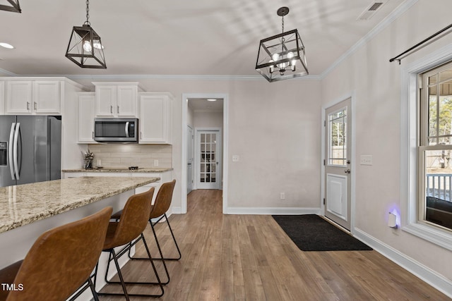 kitchen featuring white cabinetry, appliances with stainless steel finishes, decorative light fixtures, and light stone counters