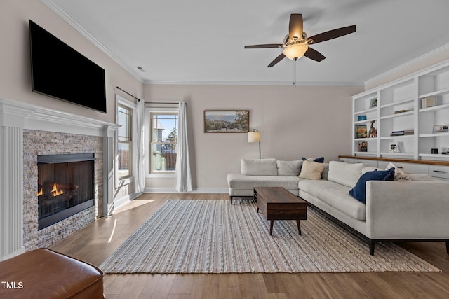 living room with a stone fireplace, ornamental molding, light hardwood / wood-style floors, and ceiling fan