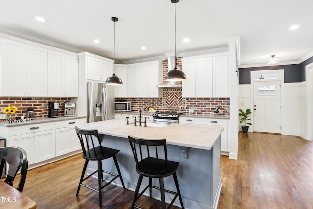 kitchen featuring wall chimney range hood, stainless steel appliances, tasteful backsplash, hanging light fixtures, and a kitchen island with sink