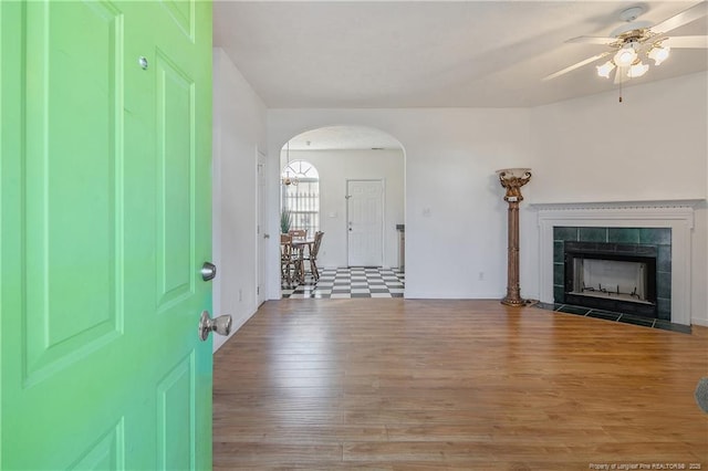 unfurnished living room featuring hardwood / wood-style flooring, ceiling fan, and a tiled fireplace