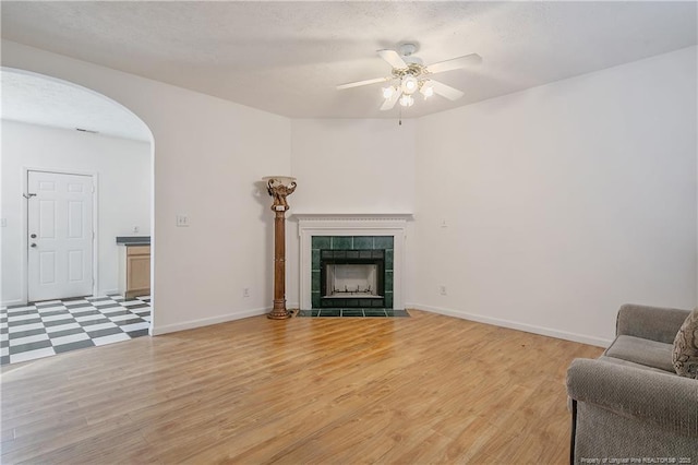 living room with ceiling fan, a tiled fireplace, and light hardwood / wood-style flooring