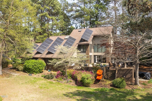 rear view of house featuring a lawn and solar panels