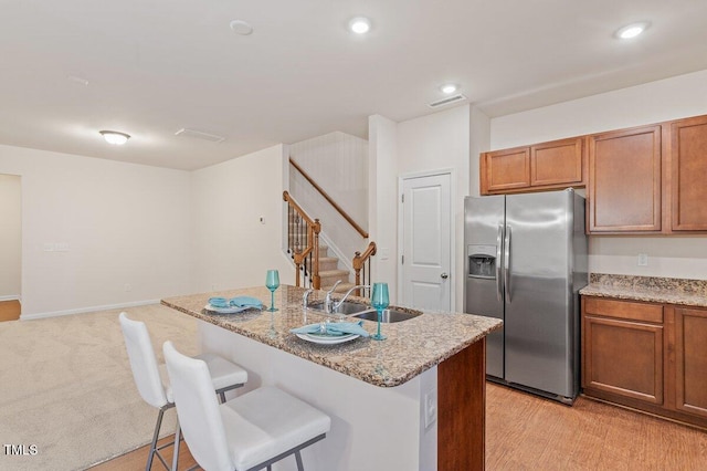 kitchen featuring stainless steel refrigerator with ice dispenser, sink, an island with sink, a breakfast bar area, and light stone counters