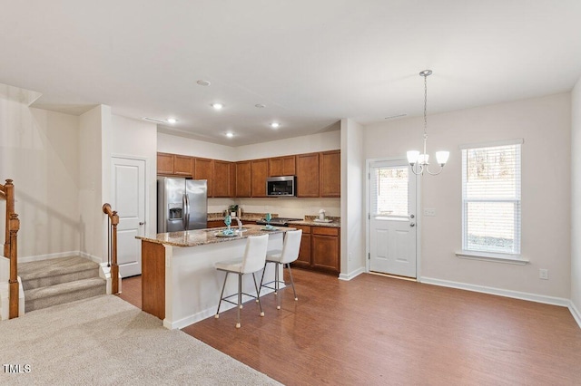 kitchen with appliances with stainless steel finishes, decorative light fixtures, a kitchen breakfast bar, a kitchen island with sink, and light stone counters