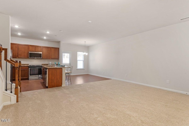 kitchen with a breakfast bar area, carpet, appliances with stainless steel finishes, hanging light fixtures, and a kitchen island