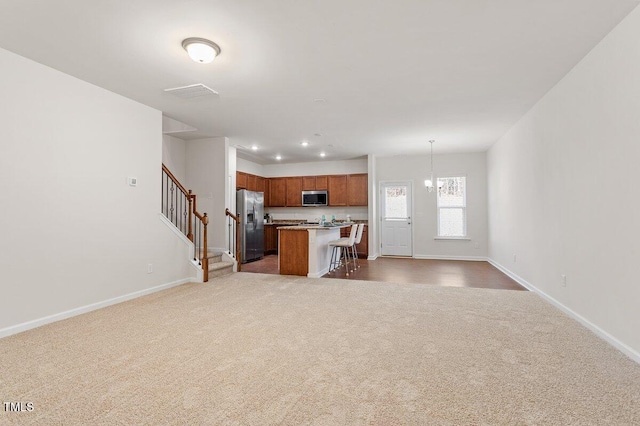 kitchen featuring a breakfast bar area, appliances with stainless steel finishes, light colored carpet, pendant lighting, and a center island