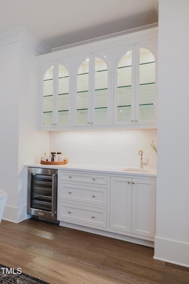 bar with beverage cooler, dark wood-type flooring, white cabinetry, sink, and backsplash