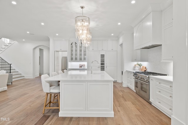 kitchen with double oven range, sink, a kitchen island with sink, and custom exhaust hood