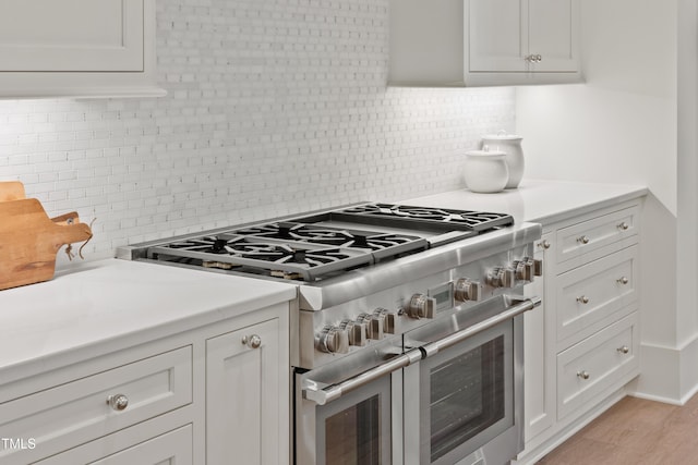 kitchen featuring white cabinetry, range with two ovens, light wood-type flooring, and tasteful backsplash