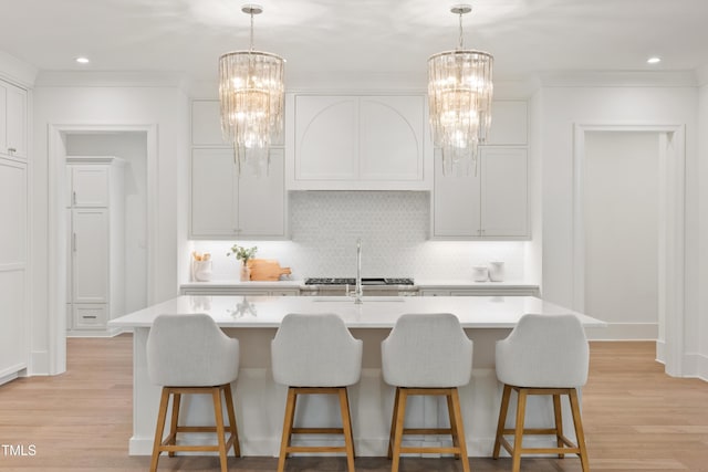 kitchen with light wood-type flooring, a kitchen island with sink, tasteful backsplash, and white cabinetry