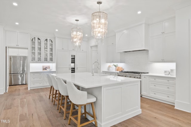 kitchen with white cabinetry, appliances with stainless steel finishes, a kitchen island with sink, light wood-type flooring, and sink