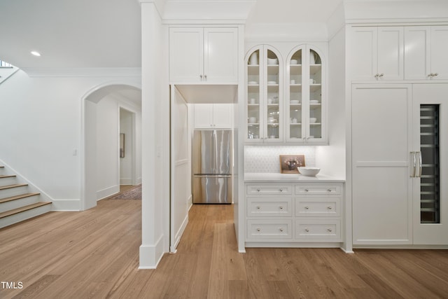 kitchen with light wood-type flooring, white cabinets, backsplash, and stainless steel refrigerator