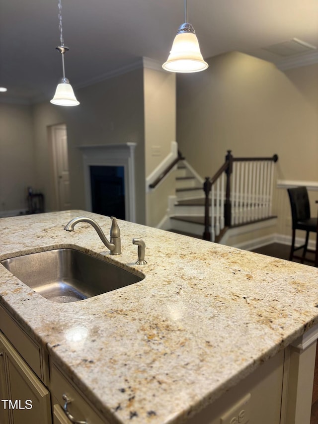 kitchen with ornamental molding, pendant lighting, light stone counters, and sink