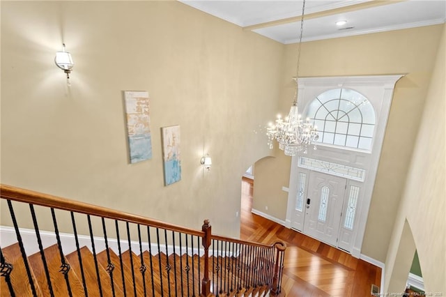 entrance foyer featuring hardwood / wood-style flooring, ornamental molding, a chandelier, and a towering ceiling