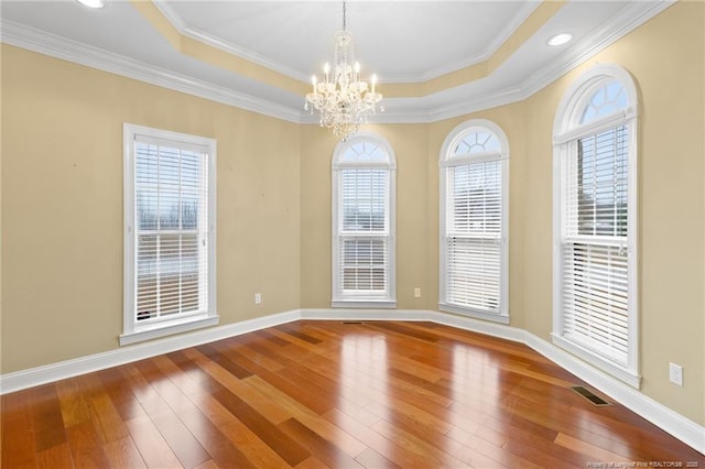 spare room with an inviting chandelier, hardwood / wood-style floors, a tray ceiling, and crown molding