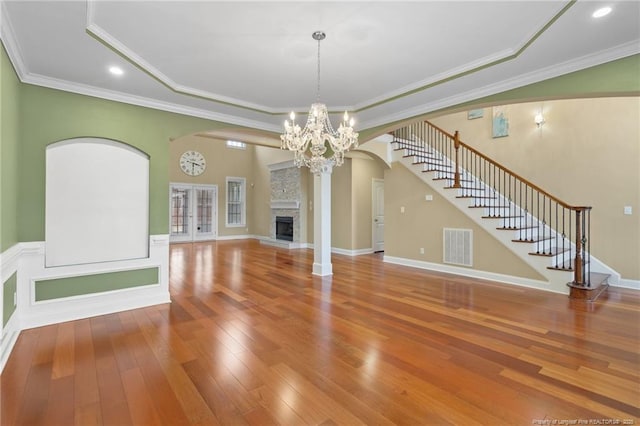 unfurnished living room featuring crown molding, a stone fireplace, a raised ceiling, and hardwood / wood-style flooring