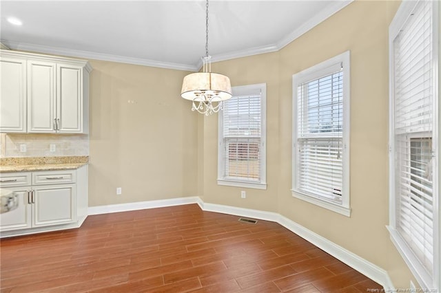 unfurnished dining area with crown molding, an inviting chandelier, and hardwood / wood-style flooring