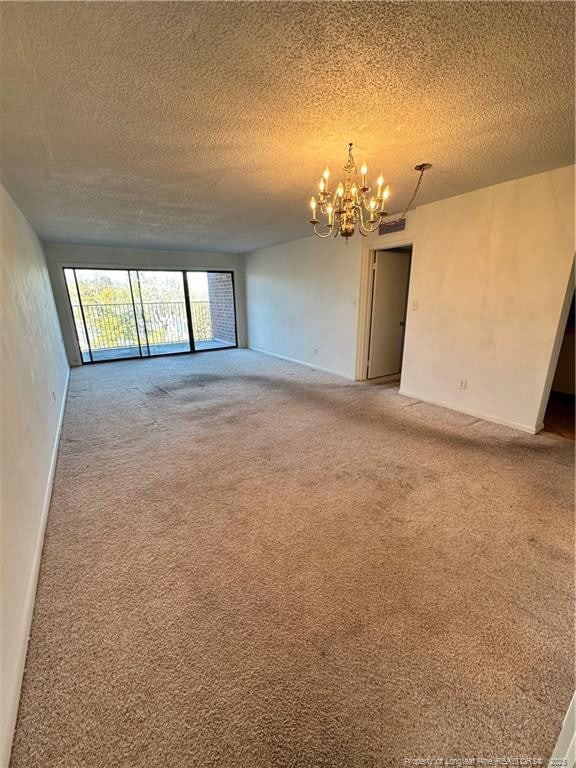 spare room with a textured ceiling, a chandelier, and carpet