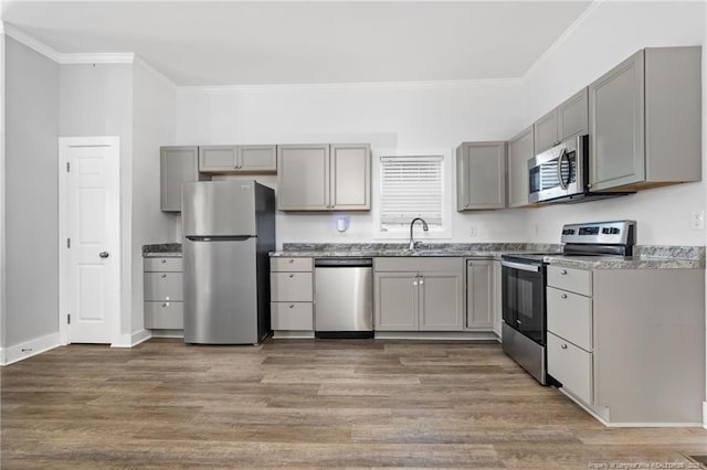 kitchen featuring appliances with stainless steel finishes, gray cabinetry, wood-type flooring, crown molding, and sink