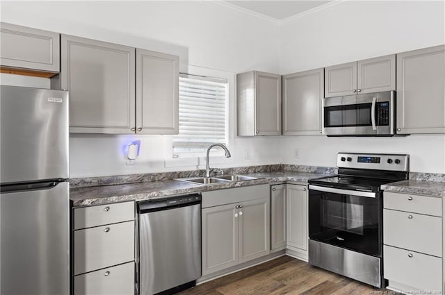 kitchen featuring sink, appliances with stainless steel finishes, gray cabinetry, ornamental molding, and dark hardwood / wood-style flooring