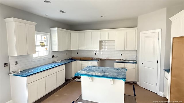 kitchen with tasteful backsplash, visible vents, white cabinetry, and a center island