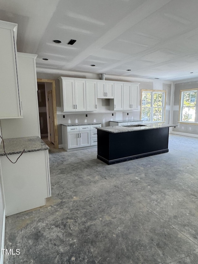 kitchen featuring stone countertops, white cabinetry, a sink, and a center island