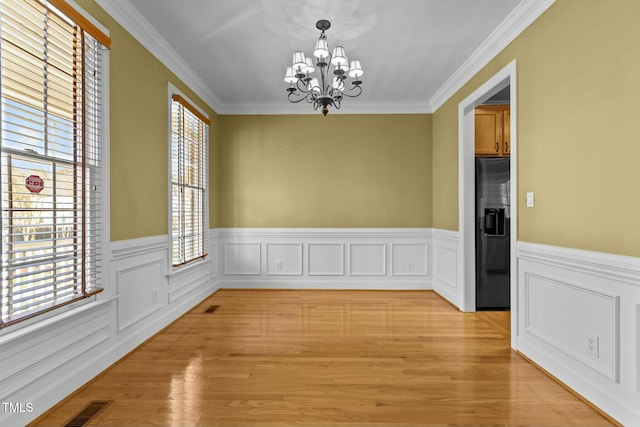 unfurnished dining area featuring crown molding, a chandelier, and light wood-type flooring