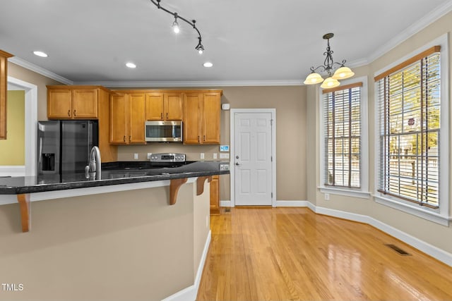 kitchen featuring pendant lighting, a breakfast bar area, appliances with stainless steel finishes, dark stone countertops, and ornamental molding