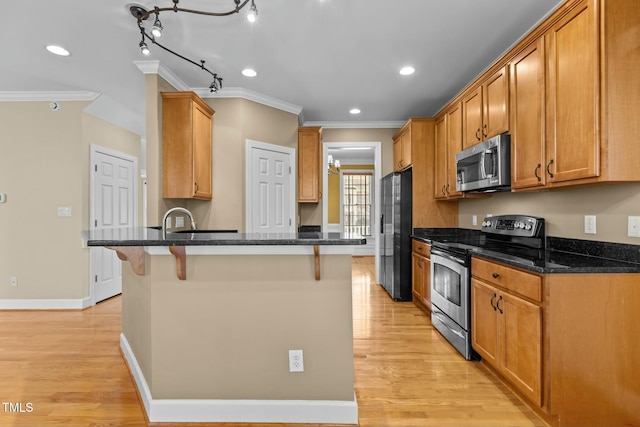 kitchen with dark stone countertops, stainless steel appliances, light hardwood / wood-style floors, and a kitchen bar