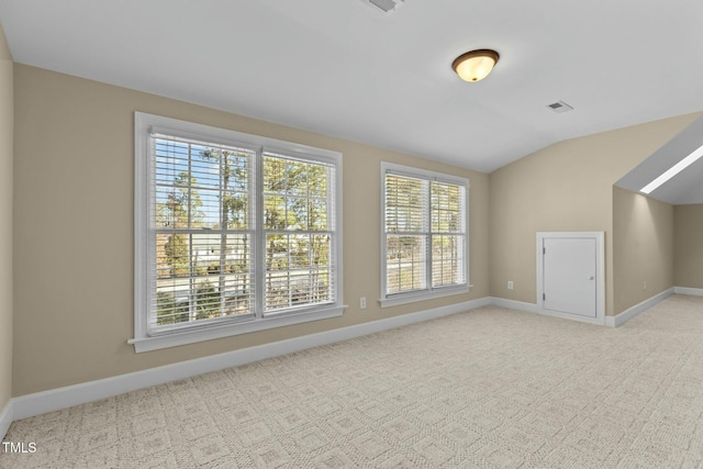 unfurnished room with a wealth of natural light, vaulted ceiling, and light colored carpet