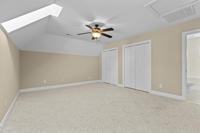 unfurnished bedroom featuring lofted ceiling with skylight, two closets, light colored carpet, and ensuite bath