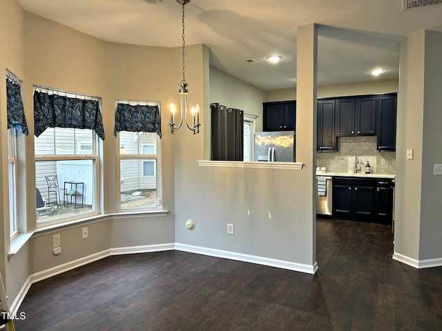 interior space featuring dark wood-type flooring, decorative light fixtures, appliances with stainless steel finishes, a notable chandelier, and backsplash