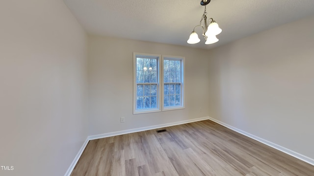 empty room featuring a textured ceiling, light hardwood / wood-style flooring, and a notable chandelier