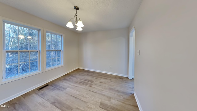 unfurnished dining area featuring a textured ceiling, light hardwood / wood-style flooring, and a notable chandelier