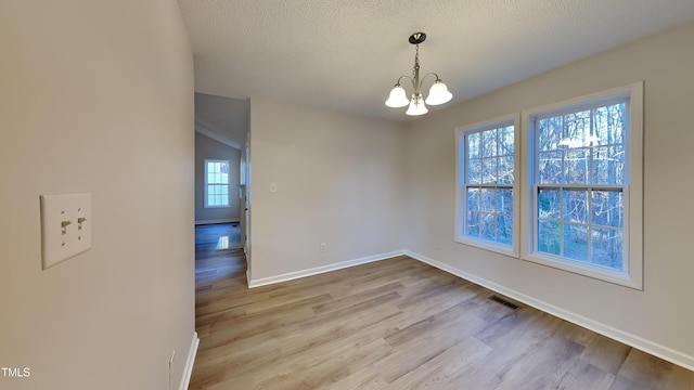 unfurnished dining area featuring a textured ceiling, light hardwood / wood-style flooring, a notable chandelier, and a healthy amount of sunlight