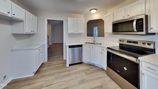 kitchen featuring stainless steel appliances, light wood-type flooring, a textured ceiling, white cabinets, and sink