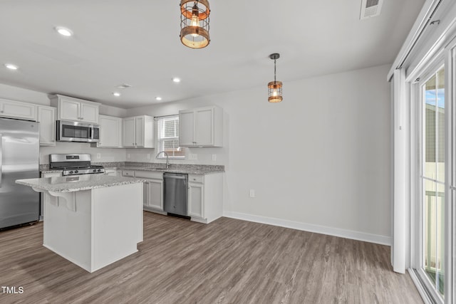 kitchen with a center island, pendant lighting, stainless steel appliances, light hardwood / wood-style floors, and white cabinets