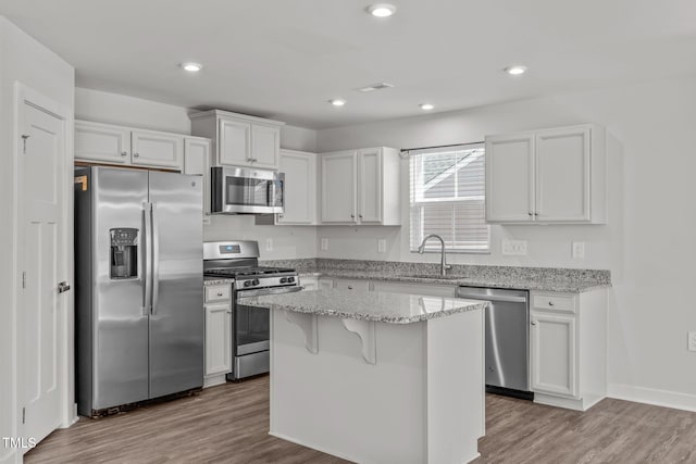 kitchen with sink, white cabinetry, stainless steel appliances, a center island, and light stone countertops