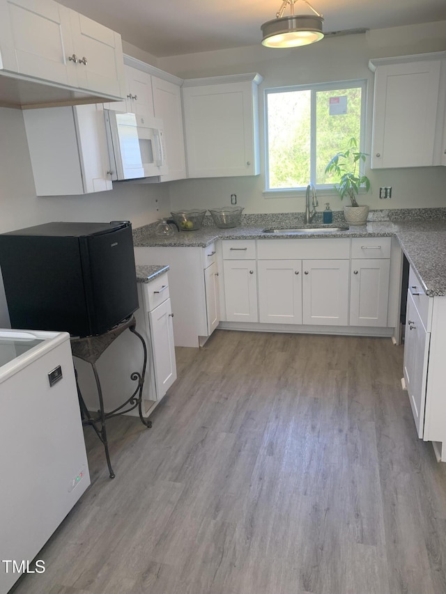 kitchen with light wood-type flooring, light stone countertops, sink, and white cabinets