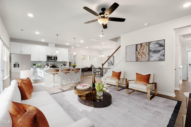 living room with ceiling fan with notable chandelier and light hardwood / wood-style floors