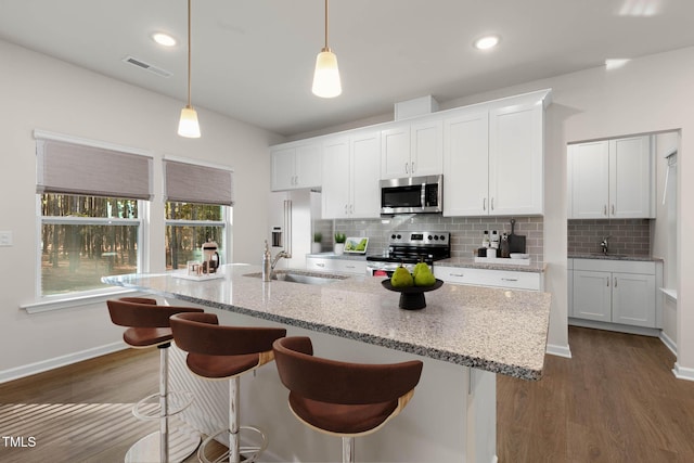 kitchen featuring a center island with sink, appliances with stainless steel finishes, hanging light fixtures, white cabinets, and sink