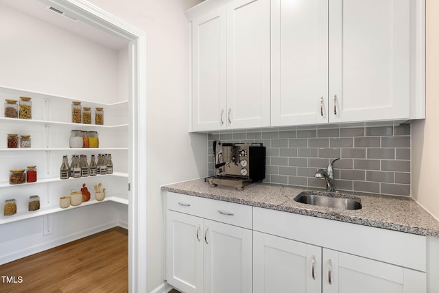 bar with light wood-type flooring, white cabinetry, light stone counters, and sink