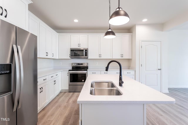 kitchen featuring decorative light fixtures, white cabinetry, stainless steel appliances, sink, and a center island with sink