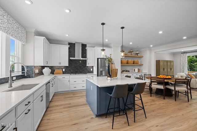 kitchen featuring a kitchen bar, sink, white cabinetry, stainless steel appliances, and wall chimney range hood