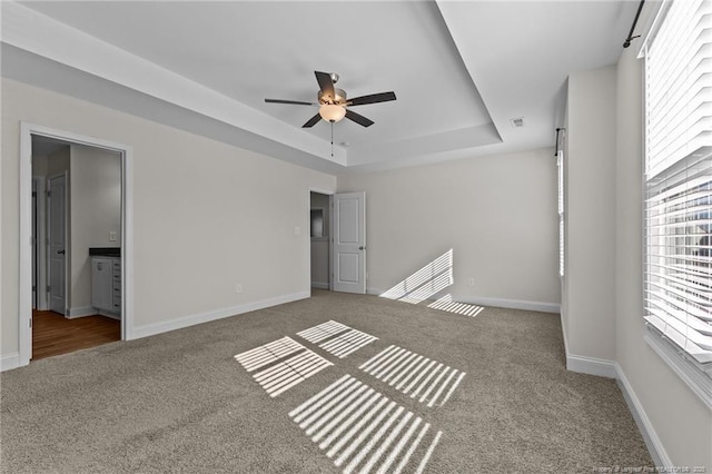 interior space featuring ceiling fan, a raised ceiling, ensuite bath, and carpet floors