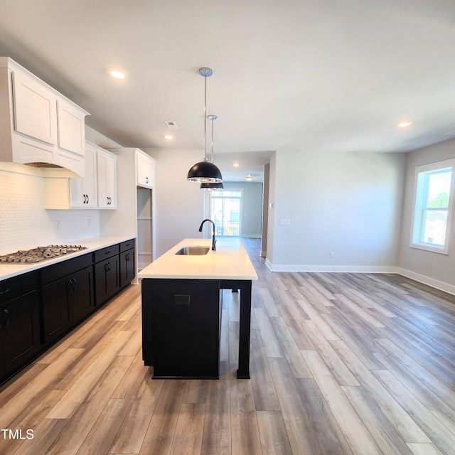 kitchen featuring white cabinets, sink, hanging light fixtures, stainless steel gas stovetop, and a center island with sink